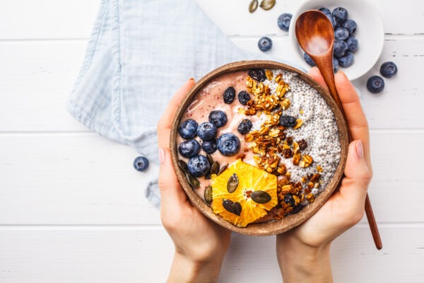 Breakfast Smoothie Bowl With Chia Pudding, Berries And Granola In A Coconut Shell On White Wooden Background.