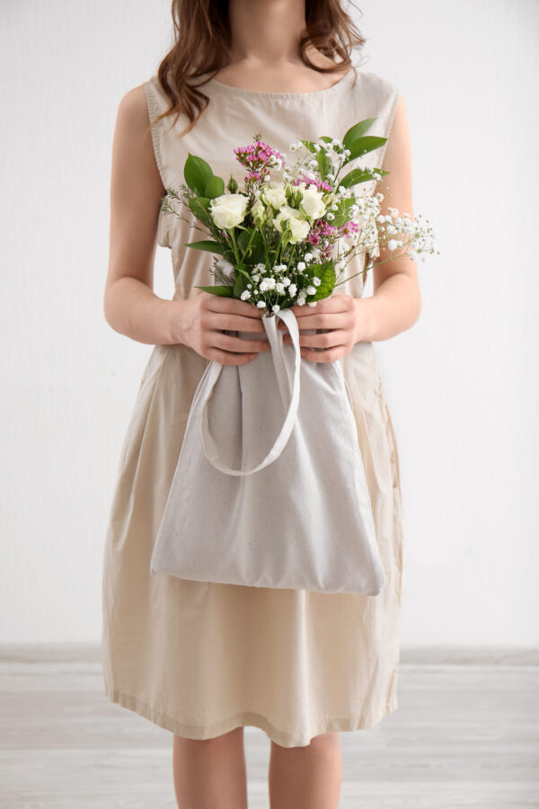 Young Woman With Bouquet Of Flowers In Eco Bag Indoors